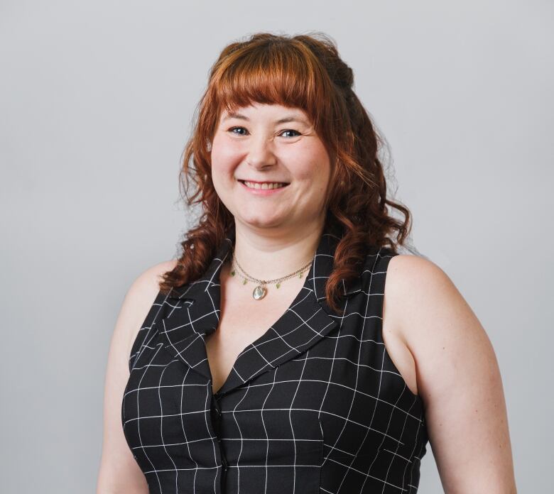 A woman with red hair and a black sleeveless dress smiles.