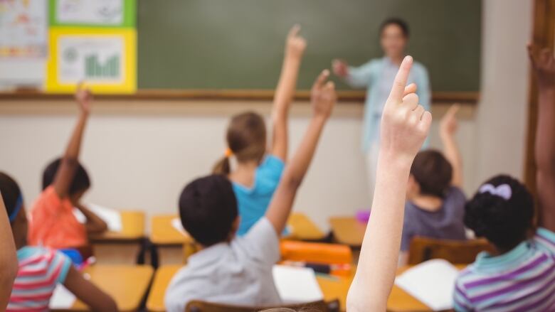 Kids in a classroom with their hands raised