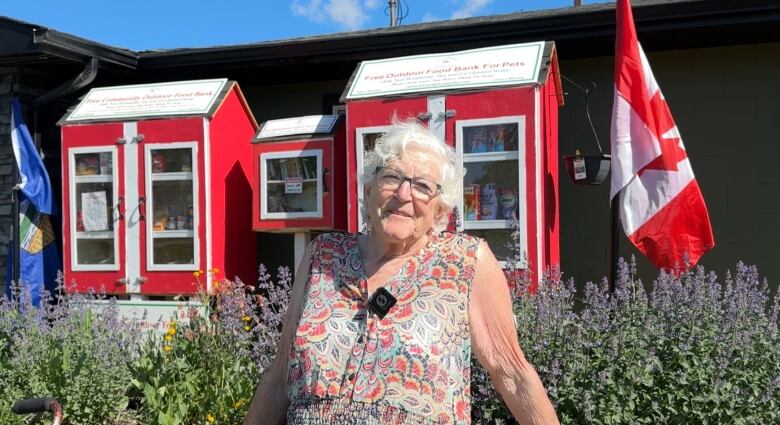 Nancy Kearny sits on the edge of a flower bed in front of a food bank and new pet food bank.