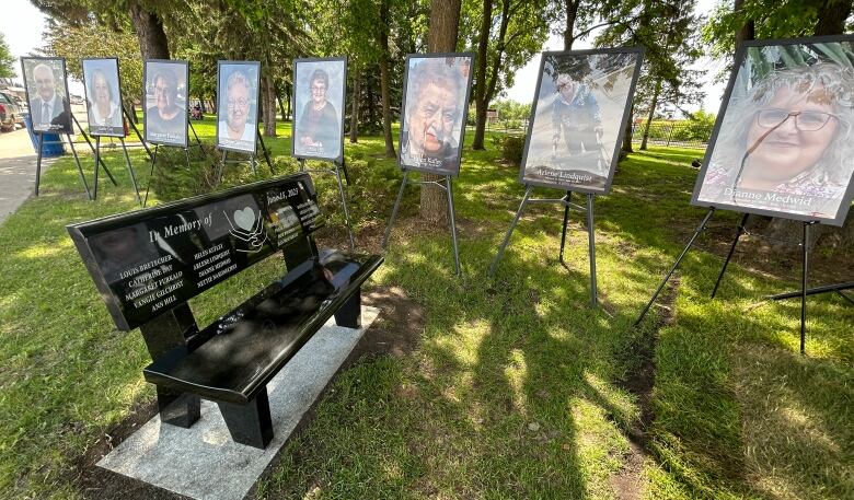 A black engraved bench sits in a park next to several large portraits of elderly people.