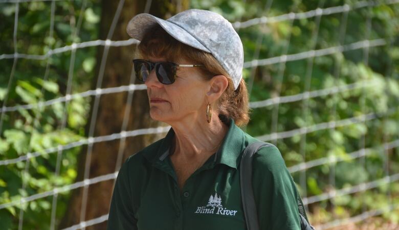 A woman wearing a hat and a green shirt reading 'Blind River'