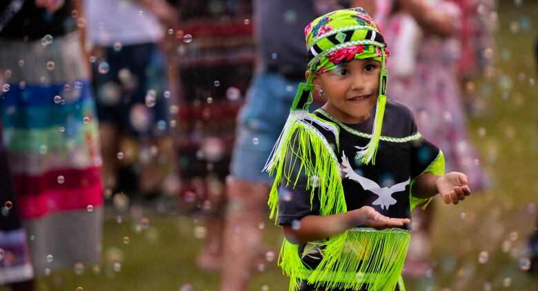 A child holds his hands out amid a cloud of bubbles.