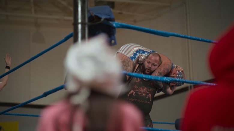 A male wrestler lifts a competitor on his shoulders He has a grimace on his face.