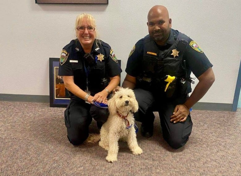 Two officers pose with a white poodle.