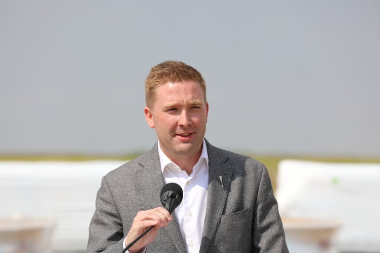 A man wearing a white dress shirt and a grey suit grasps a microphone. 