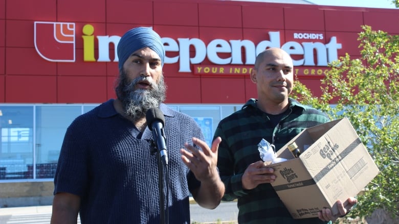 Two men outside a grocery store, one is holding a small box.