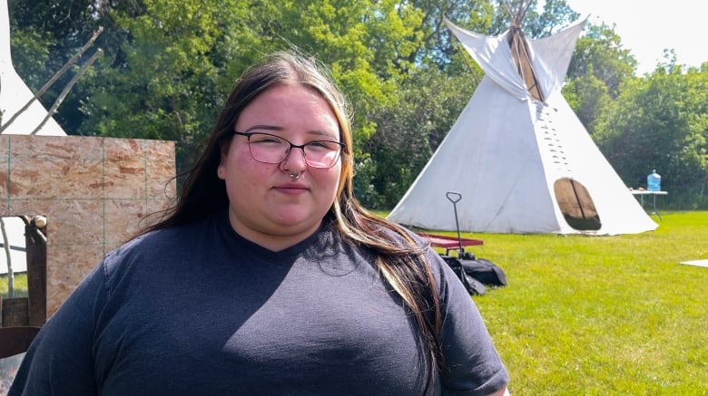 A woman sits in front of a teepee.