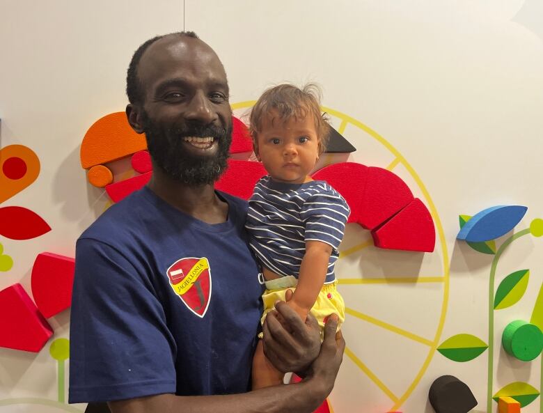 A man holds a baby in front of a decorated wall.