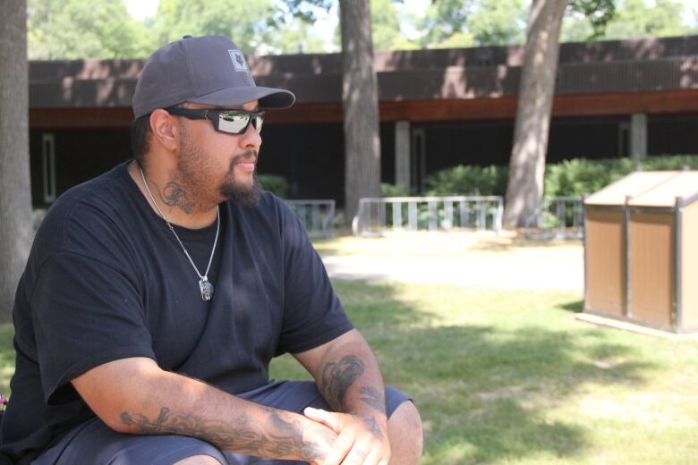 A man in a black t-shirt and dark blue shorts sits on a table, while looking forward. 