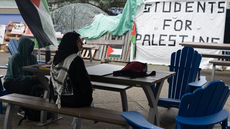 Students congregate around a picnic table facing a large white banner that says, Students for Palestine.