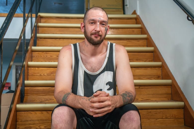 A person is seen sitting on wooden stairs with their hands folded in front of them.