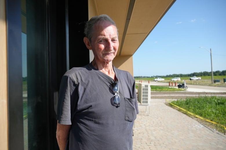 A man stands outside beside a building with sunlight streaming onto his face.