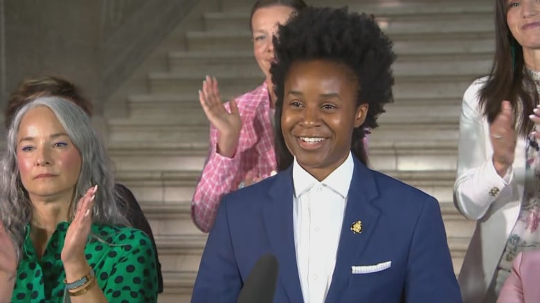 A person stands at a podium, smiling as people applaud around them