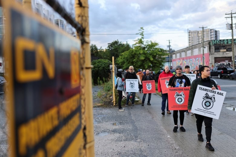 Teamsters union members picketing near a metal fence at the entrance of a lot with a sign that reads: CN provide property; no trespassing.