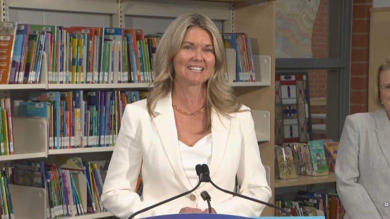 Woman in a white blazer speaking at a news conference 