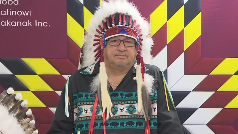 An Indigenous man wearing a headdress stands at a podium.