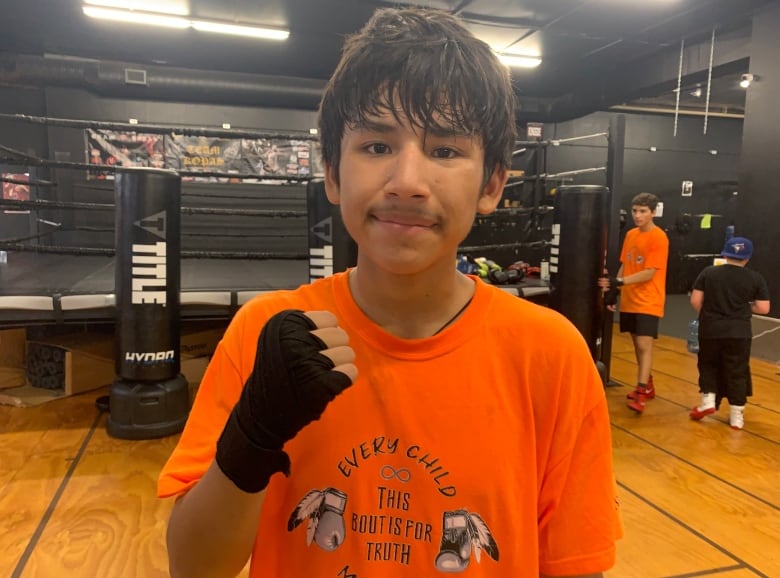 A teen boy in an orange shirt poses with a raised fist.