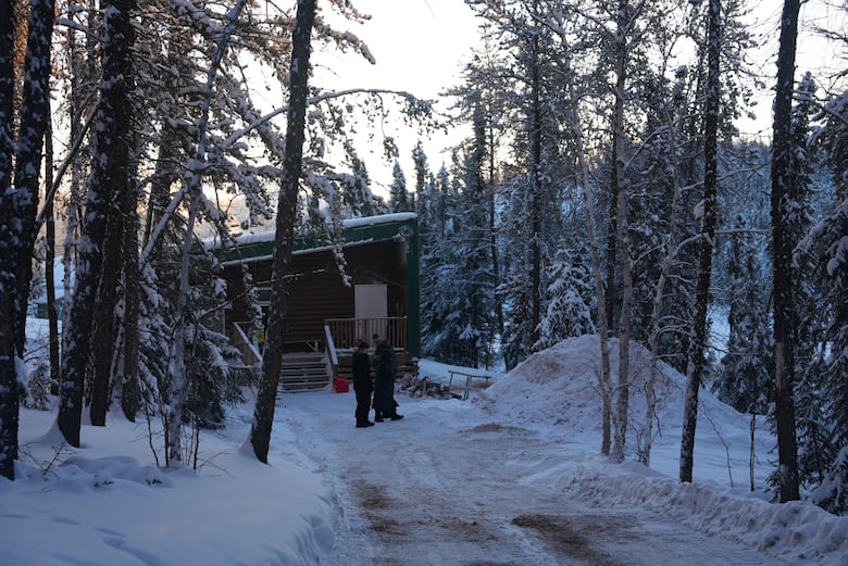 A cabin in snowy woods with two people outside