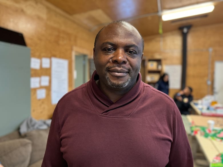 Man in burgandy sweater poses for a picture. Plywood walls in the background