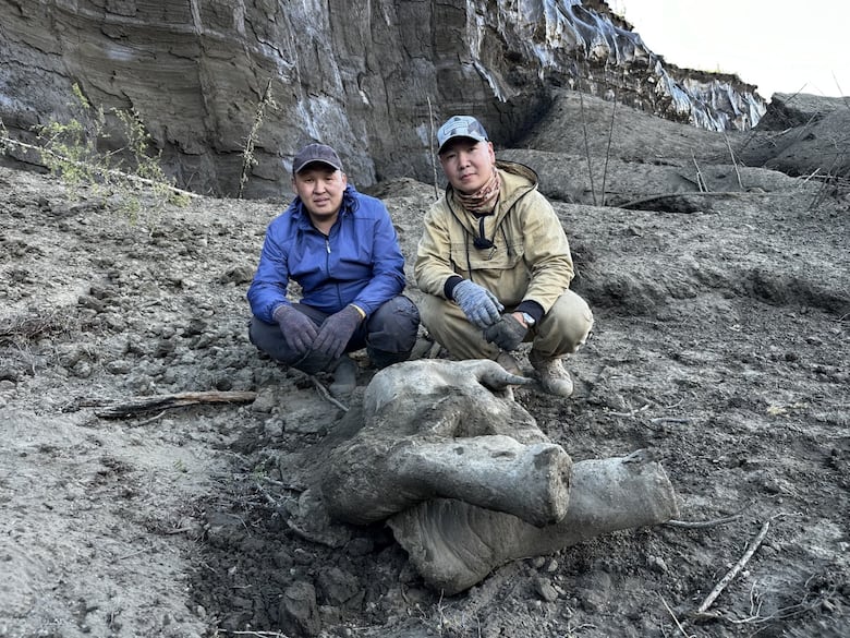 Two men pose for a picture in front of a carcass of a baby mammoth.