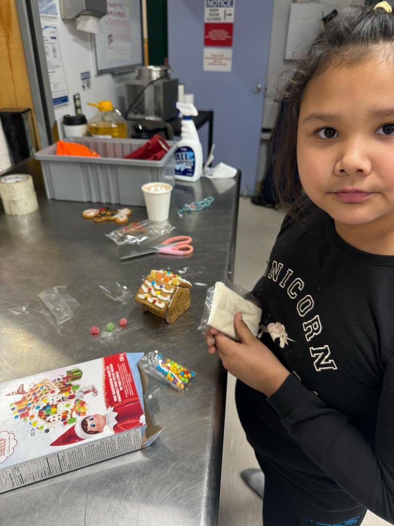 A girl stands next to a little gingerbread house.