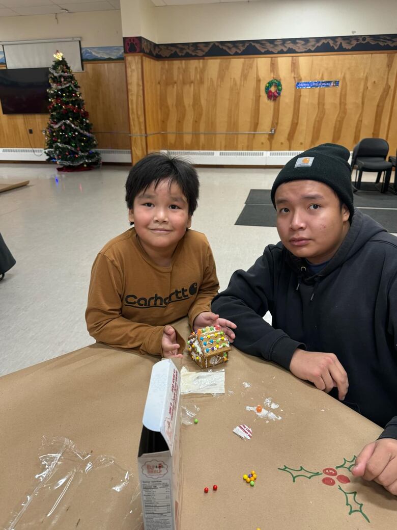 A man and a boy sit in front of a gingerbread house.